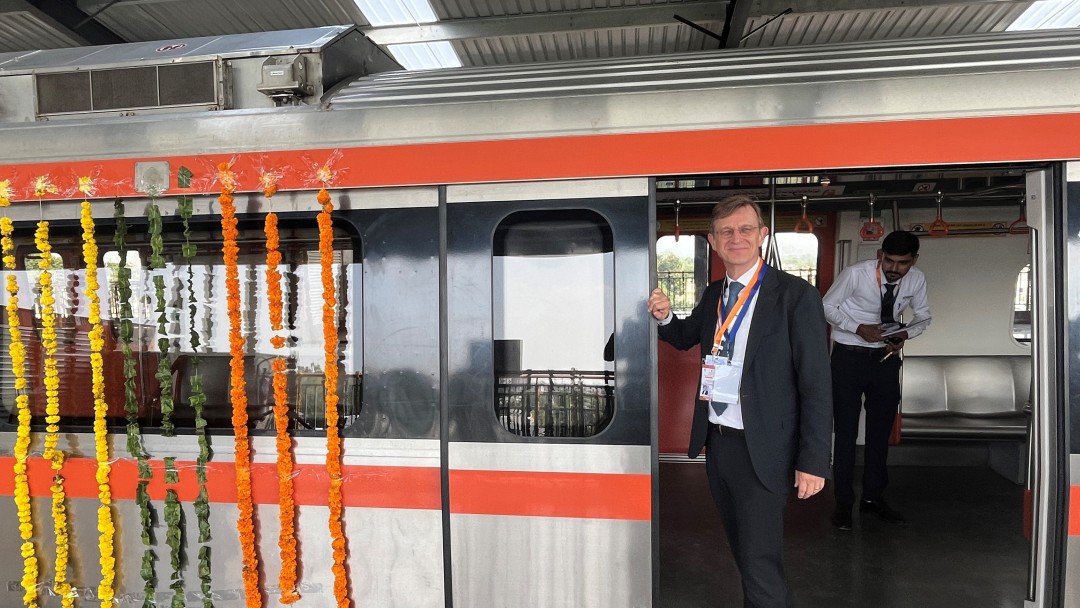 A man stands in the doorway of a railway decorated with garlands of flowers.