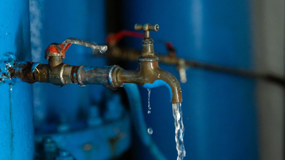 Wasser fließt aus einem Hahn in einen Plastikbecher.