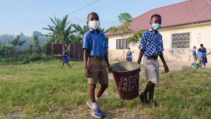 Zwei Jungs tragen gemeinsam einen Eimer, im Hintergrund der Ekoso Presby Kindergarten