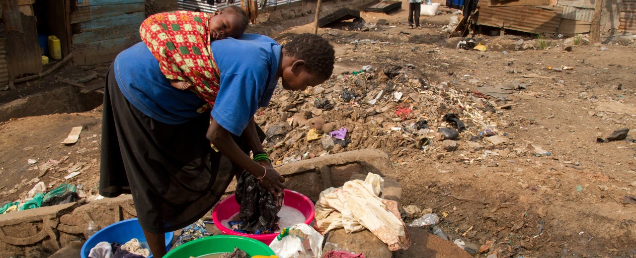 Woman with baby on her back who is washing her clothes. 