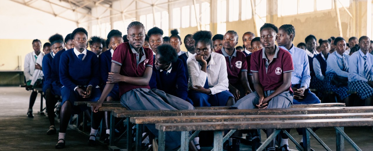 Pupils sit on benches in their school uniform.