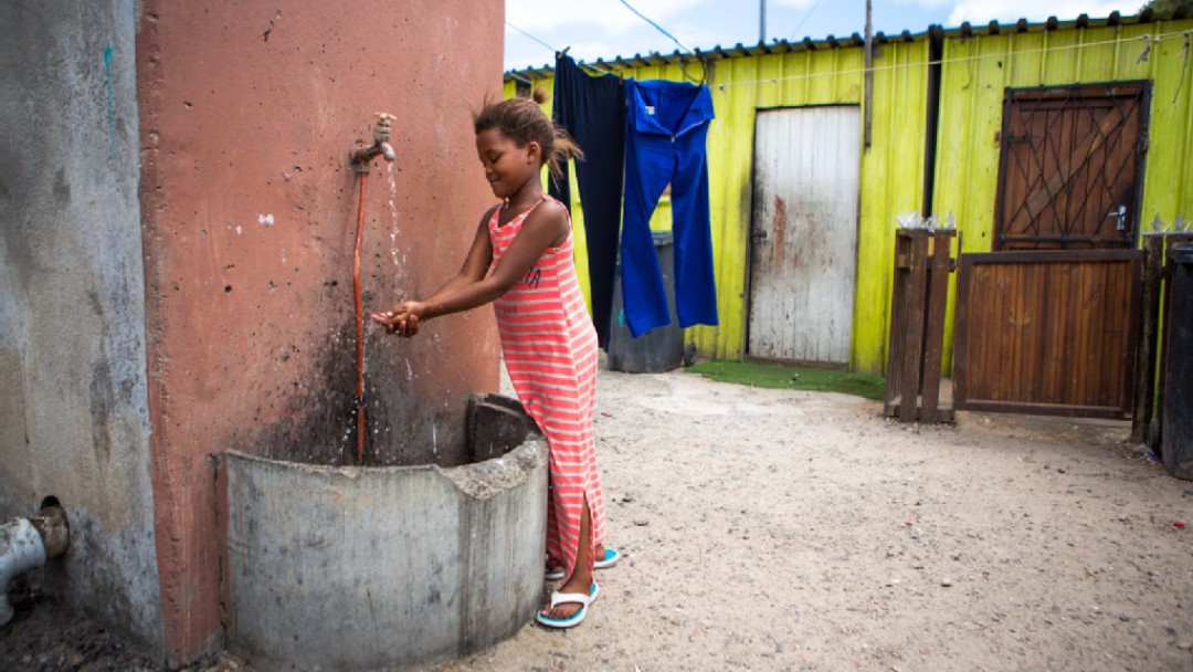 A girl washes her hands at the public water tap. 