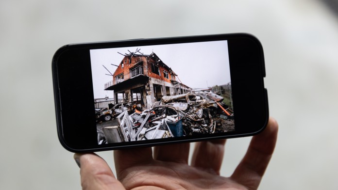 Ein Smartphone zeigt ein Bild von einer zerstörten Autowerkstatt
