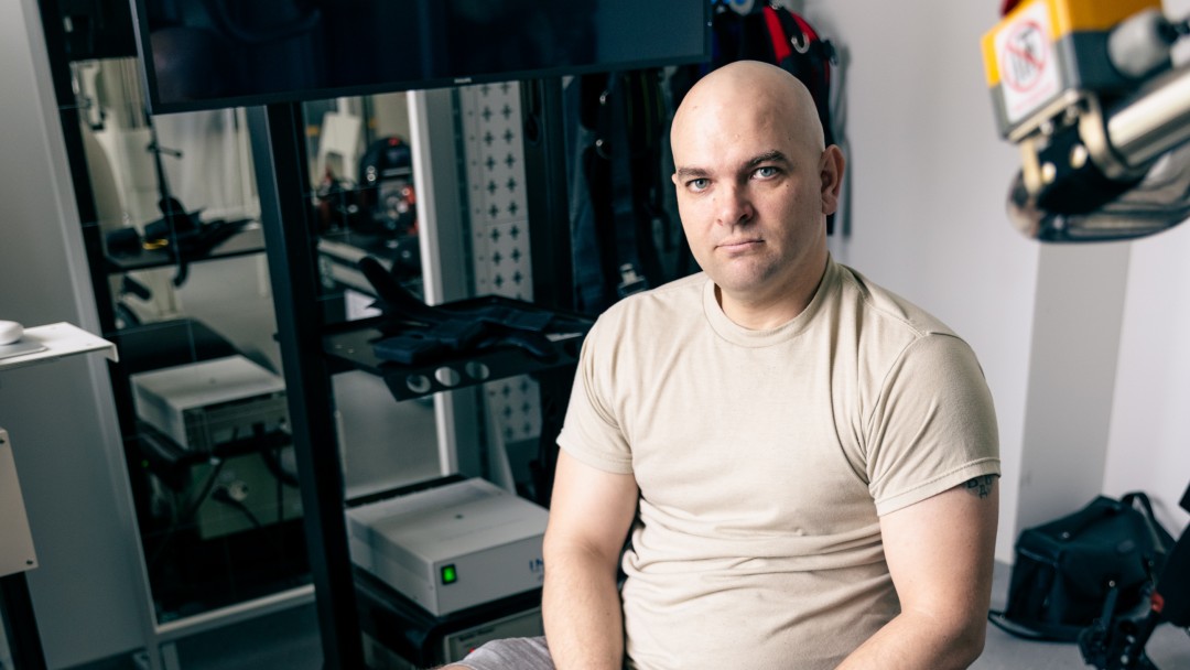 A bald man sits on an exercise machine and holds up his injured right foot.