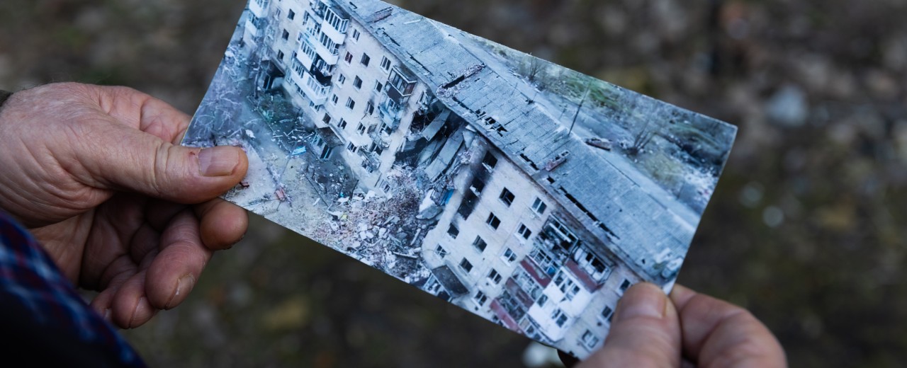 Hände halten ein Foto von einem Haus in Kyiw, dass durch den russischen Angriffskrieg zerstört wurde